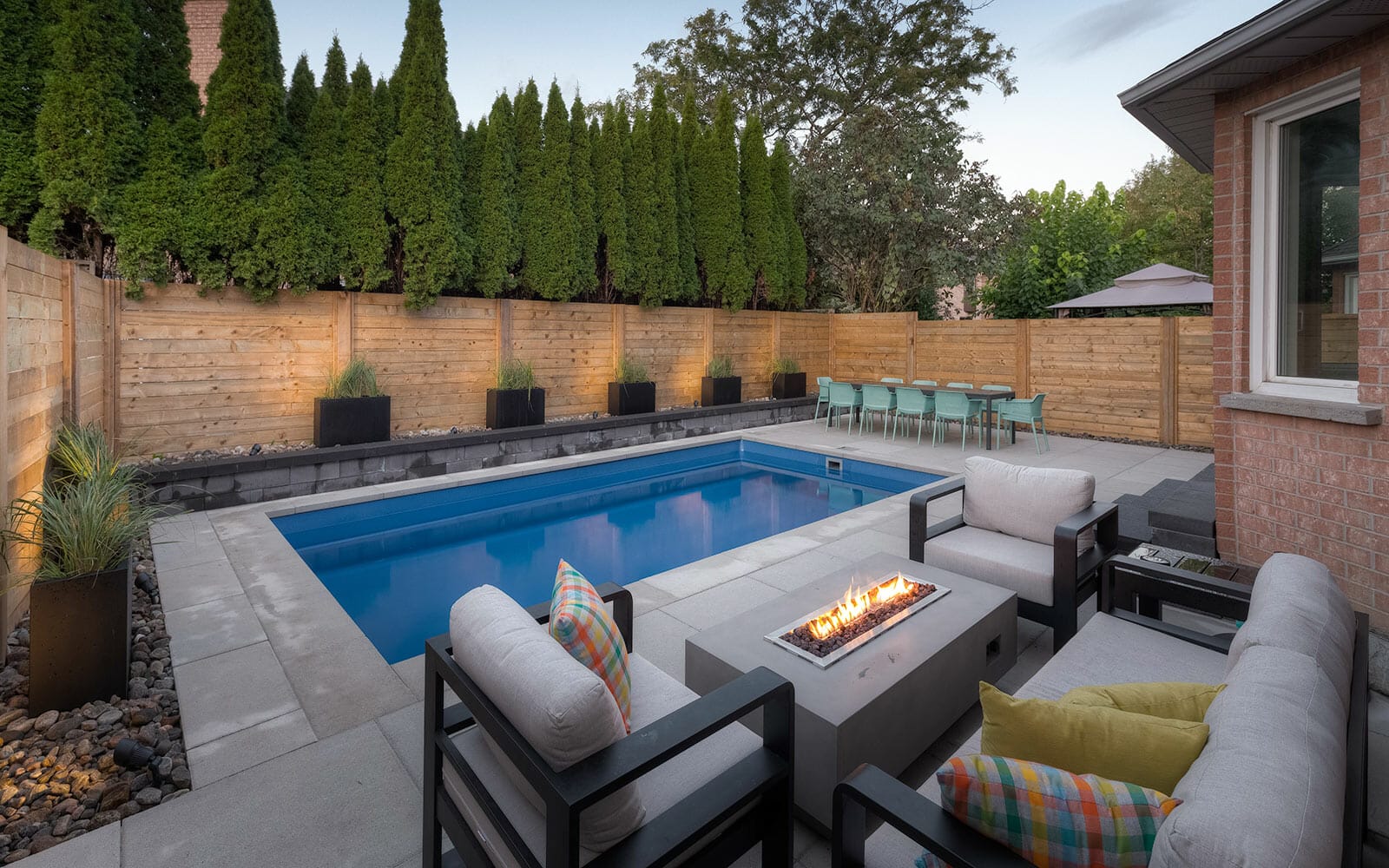 Toronto Landscape Project; Featuring Concrete Pool Installation, Cedar Privacy Fence, Outdoor Fireplace, Pool Deck Interlocking & Small Retaining Wall Around Pool Area by Toronto Landscaping Company.