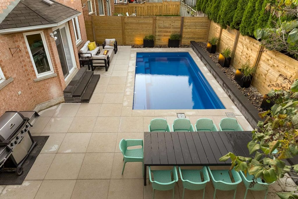 Toronto Landscaping Project for Small Toronto Backyard; Featuring Concrete Pool Installation, Interlocking, Outdoor Fireplace, Cedar Privacy Fence & Retaining Wall