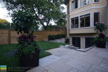 M.E. Contracting landscaping project that includes a retaining wall with lighting for flowers and plants, with a stone interlocking patio and a basement walkout.